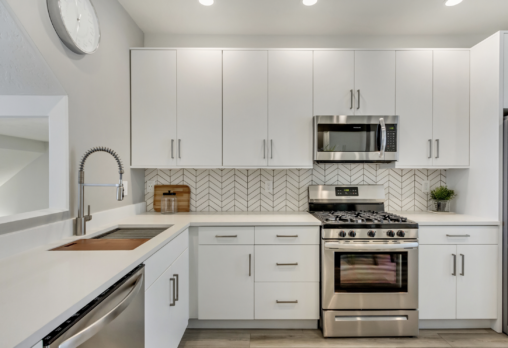 Modern kitchen with white cabinets, stainless steel appliances, chevron backsplash, and a sleek faucet.